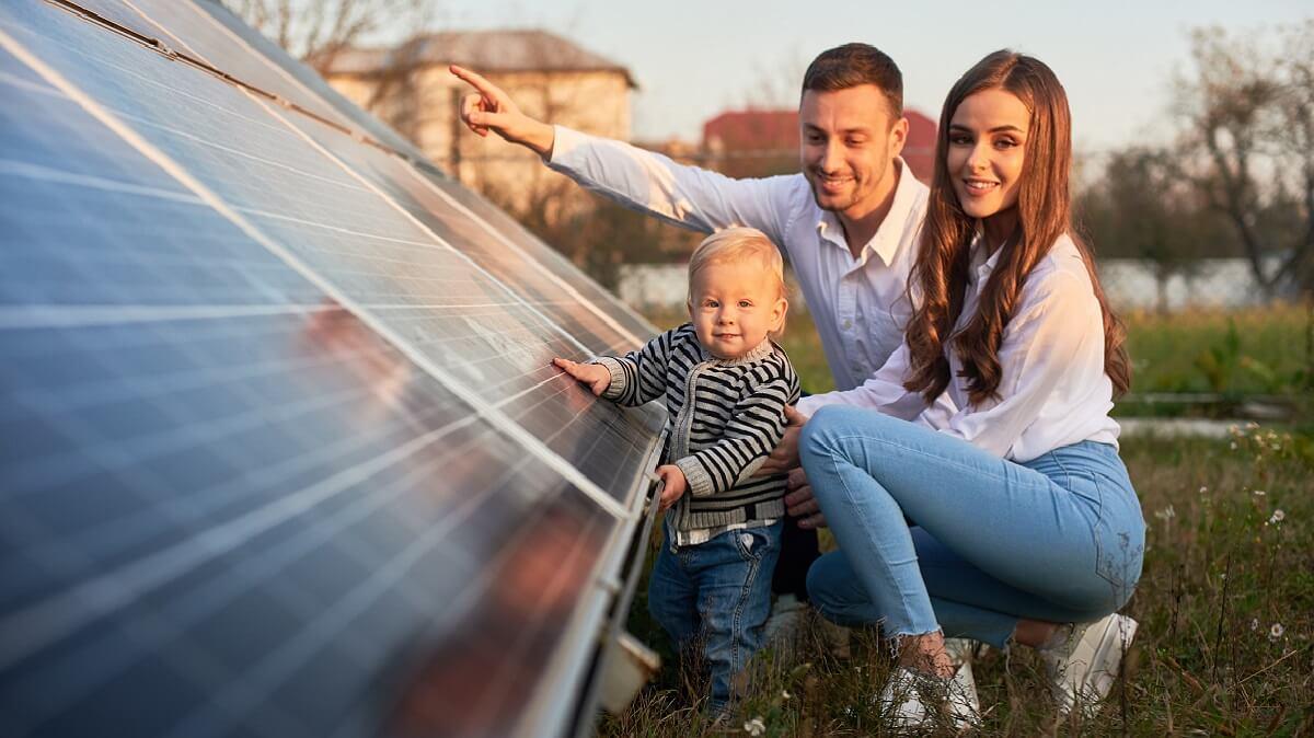 Family of three squatting next to a solar panel.