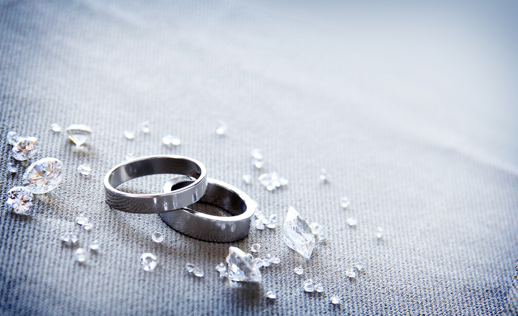 Two wedding bands lie amidst scattered crystals on a textured fabric.