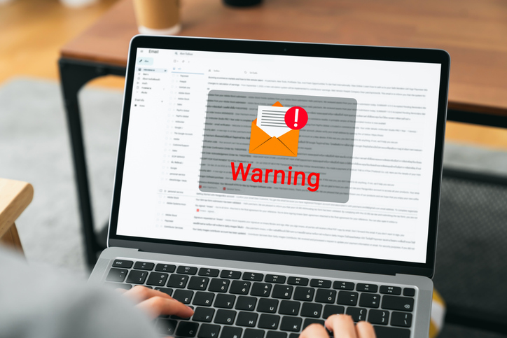 A person's view over a laptop screen displaying an email interface with a prominent "Warning" alert.